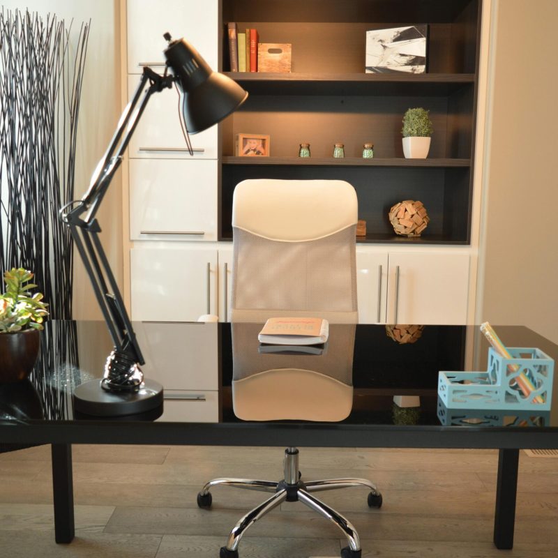 Stylish modern office workspace featuring a black desk, lamp, and white chair with shelving.